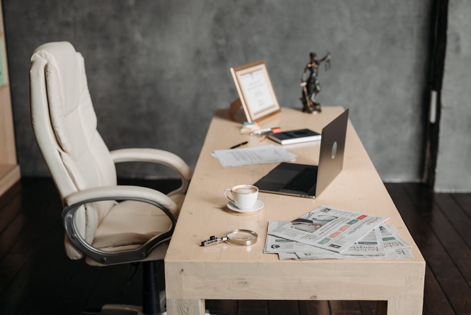 A clean office workspace featuring a cup of coffee, laptop, and newspapers on a wooden desk for a productive environment.