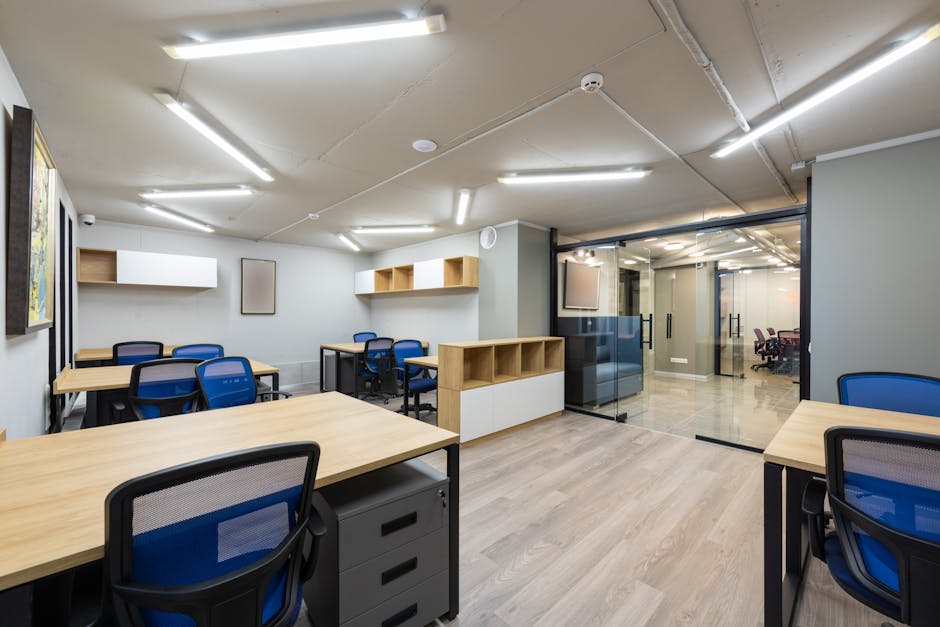 Interior of modern workplace equipped with wooden desks and blue office chairs under lamps