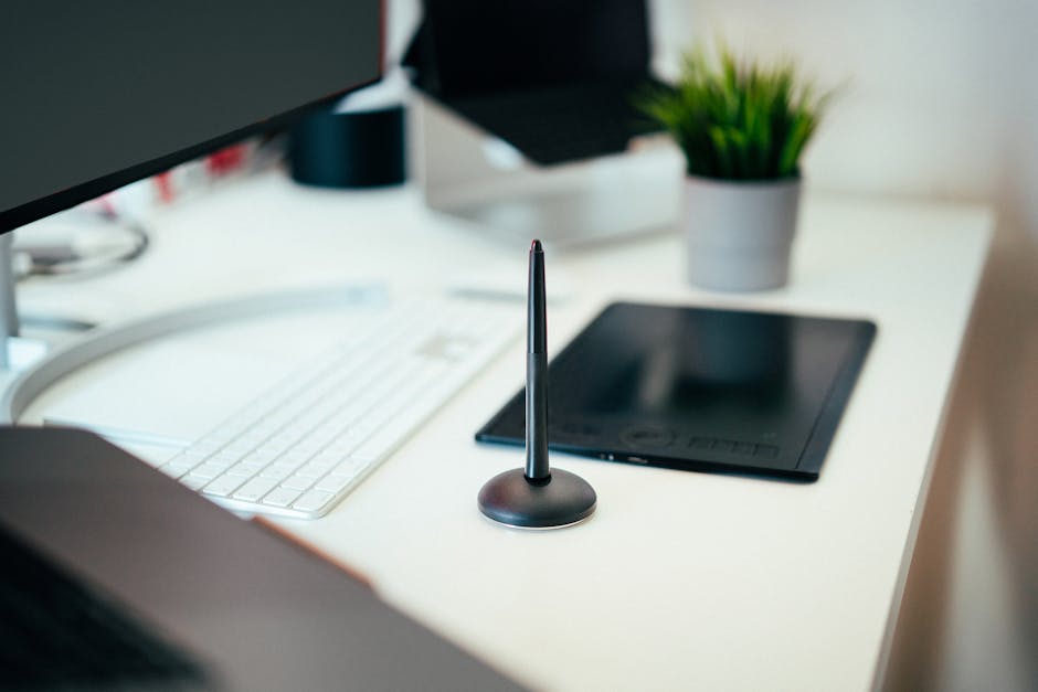 A modern workspace featuring a tablet, stylus, keyboard, monitor, and potted plant.