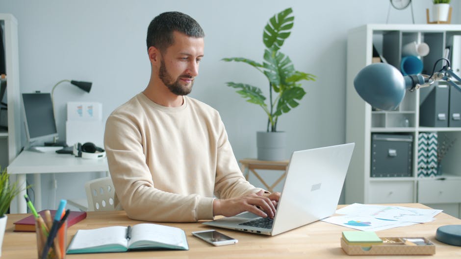 Man typing on a laptop in a modern home office setup with plants.
