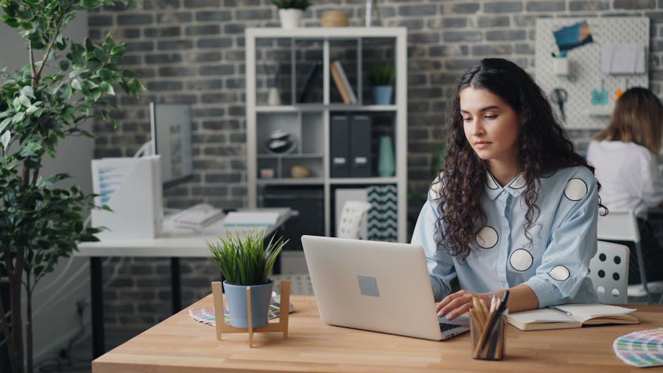 Confident young woman working on a laptop in a modern office setting, embracing creativity.