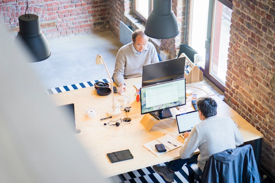 Bird's-eye view of a modern office with professionals collaborating on laptops and monitors.