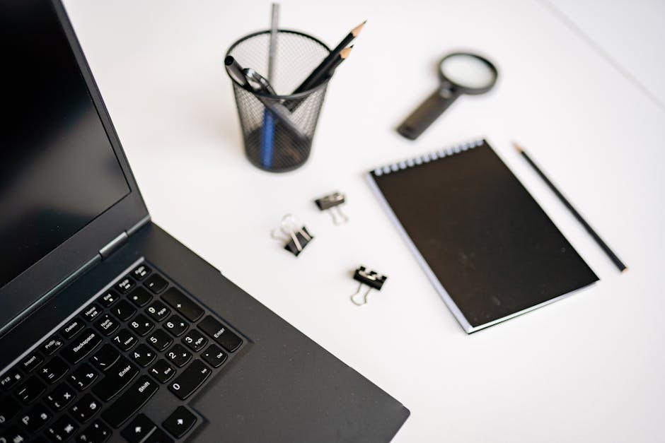 A modern office workspace featuring a laptop, notebook, and stationery on a white desk.